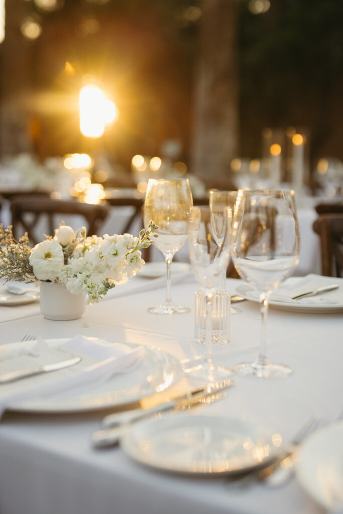 Long rectangle wedding reception table with white linens and white floral arrangements and white taper candles.