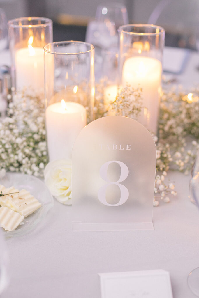 Frosted wedding table number with baby's breath and candles centerpiece behind it.