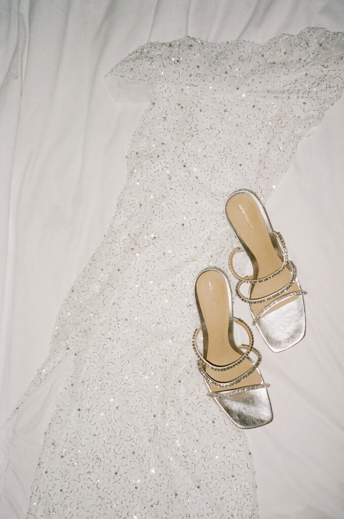 Bride's reception gown laying flat on white sheet with her shoes.