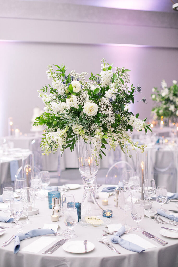 Tall reception centerpiece in glass vase of white flowers and greenery.