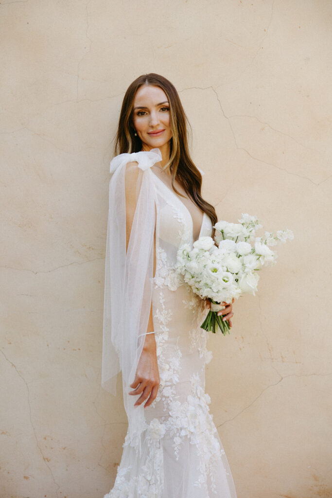 Bride smiling while looking over shoulder, holding white floral bouquet in chic gown.