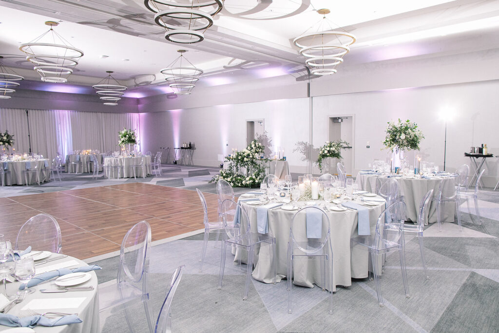 Indoor wedding reception at Mountain Shadows with round tables and clear acrylic chairs and white and soft blue linens.
