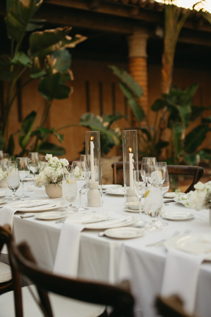 Long rectangle wedding reception table with white linens and white floral arrangements and white taper candles.