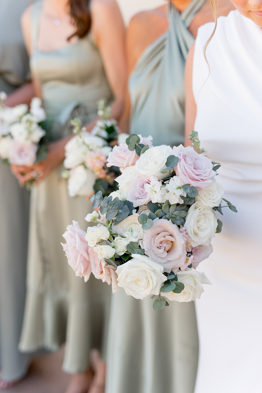 Bridal bouquet held by bride with bridesmaids in foreground in green dresses holding bouquets.