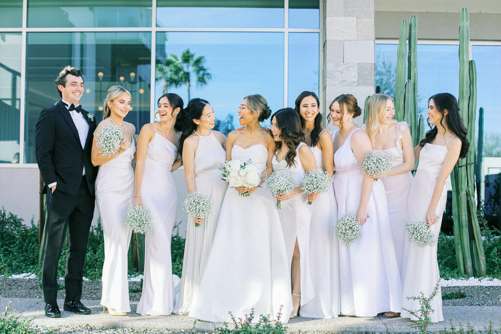 Bride with bridesmaids wearing soft pink dresses and man in black suit with bow tie.