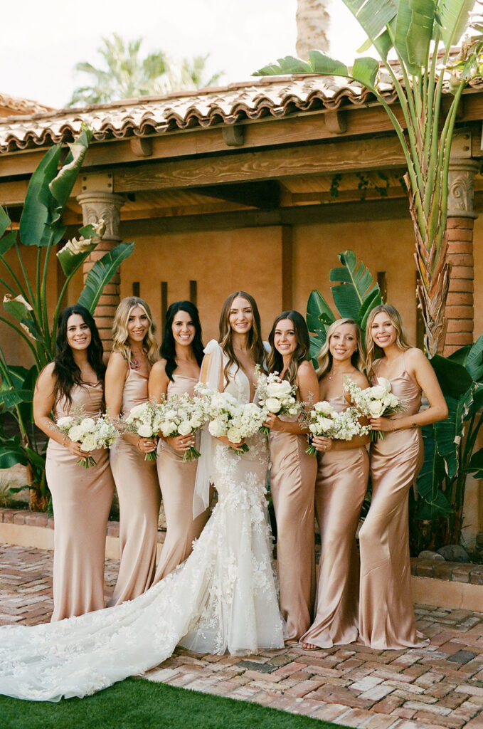 Bride standing with bridesmaids, smiling, all holding white floral bouquets at Royal Palms.