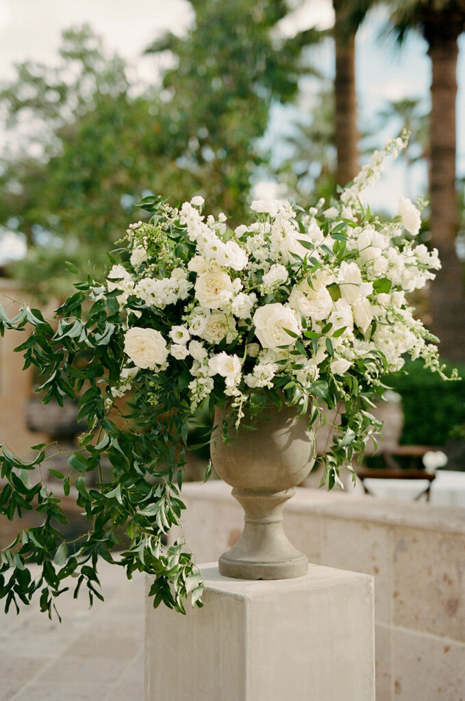 Large lush white floral and greenery arrangement on cement pillar.