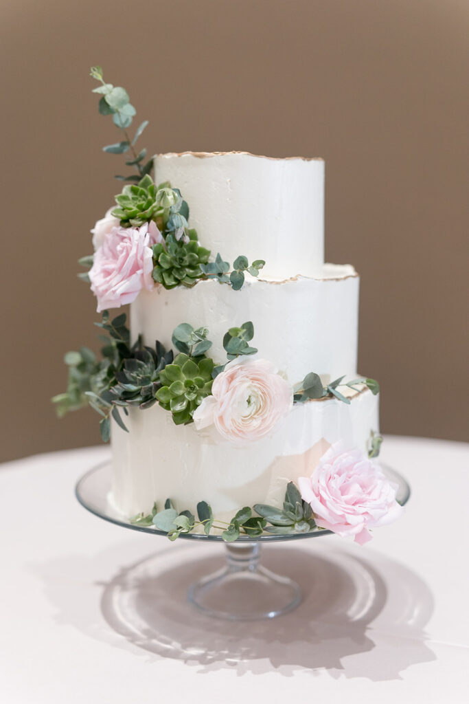 Three tiered white wedding cake with succulents, pink roses, and eucalyptus.