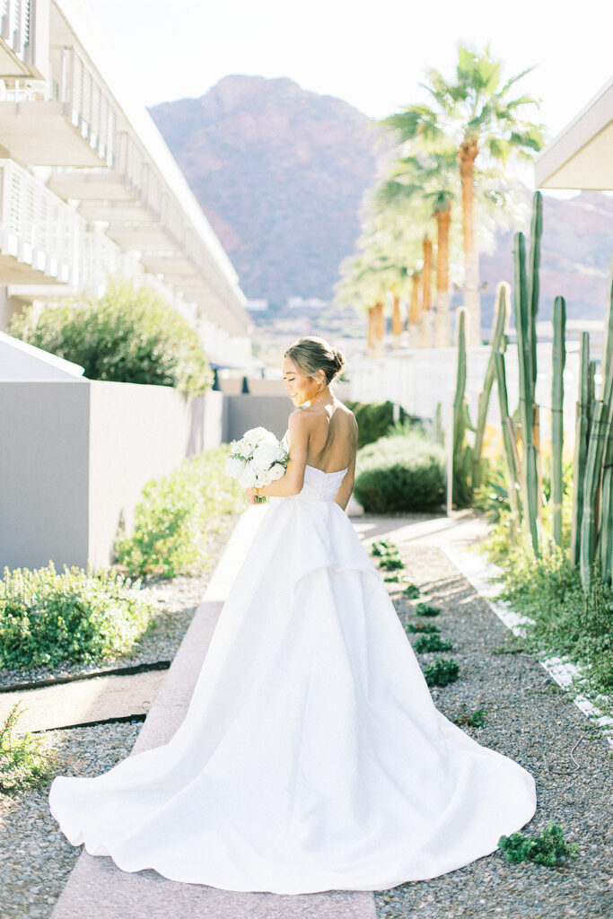 Bride standing on path looking over should and holding white floral bouquet at Mountain Shadows.