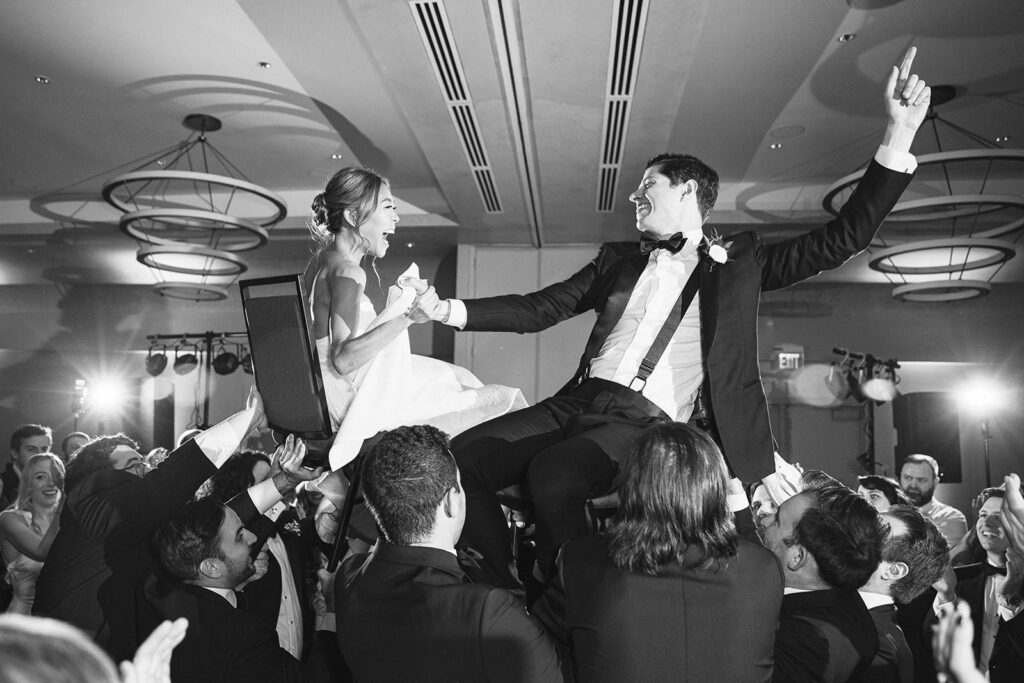 Wedding reception dance with groom and bride lifted up sitting in chairs.