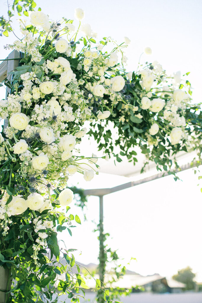 Floral installation on wedding ceremony arch of white flowers and greenery.