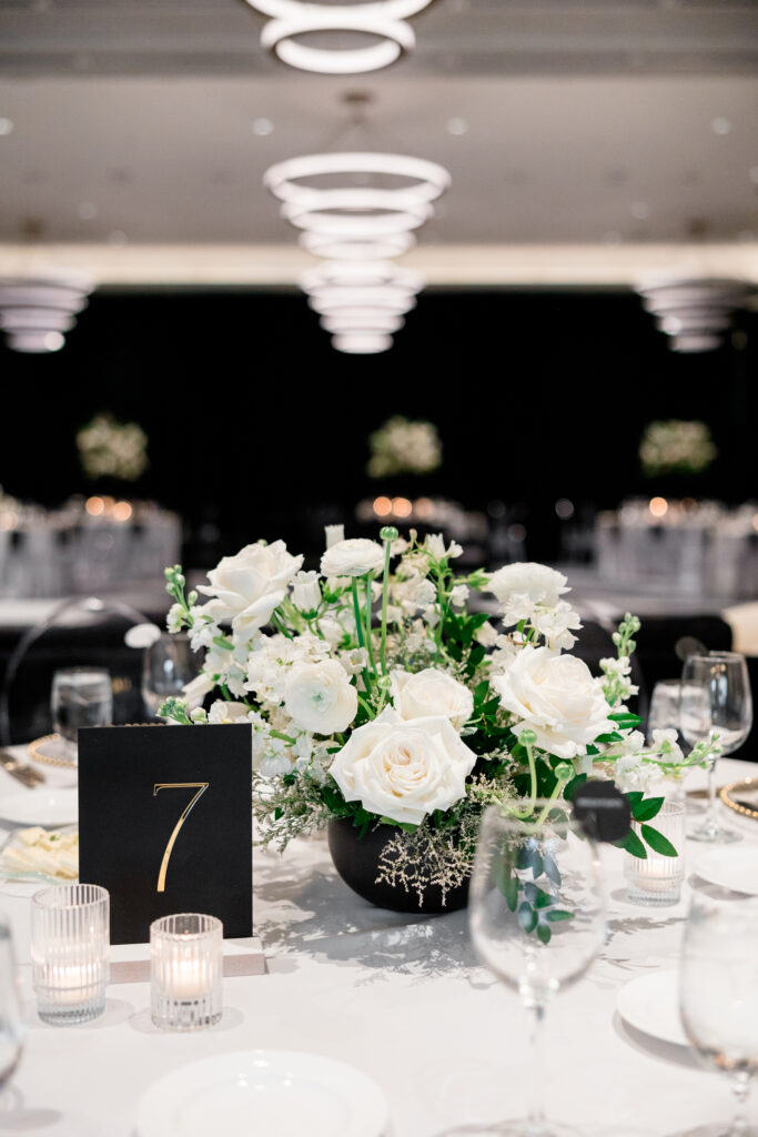 Low wedding reception centerpiece in black vase of white flowers and greenery.