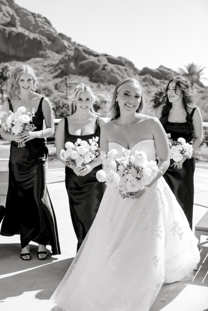 Bride smiling with bridesmaids behind her all holding bouquets of flowers.