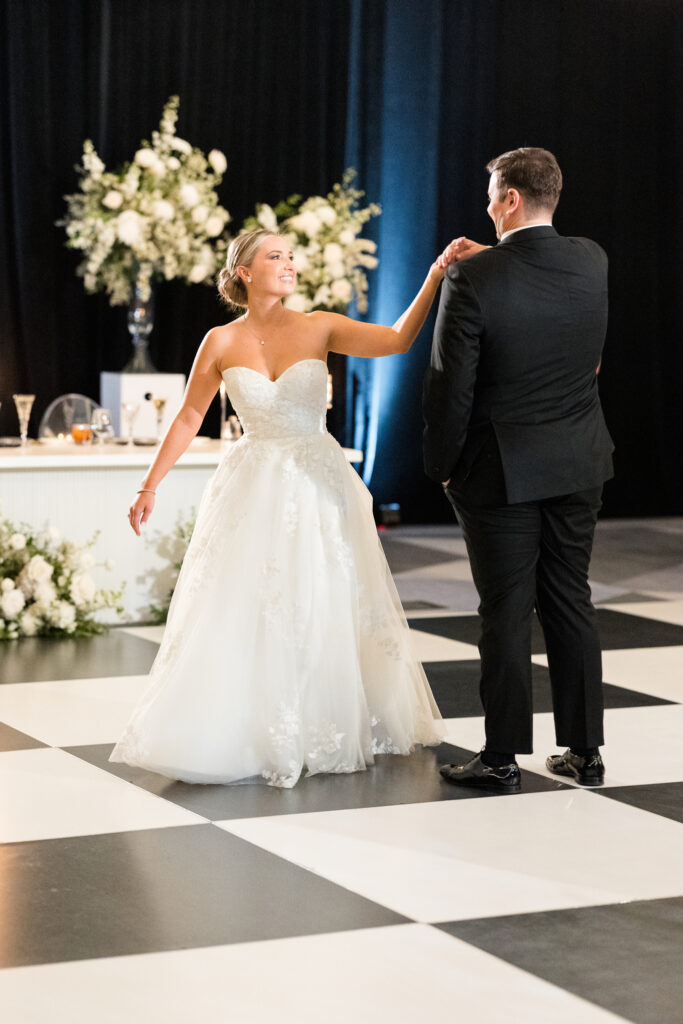 Bride and groom dancing on white and black checkered dance floor.