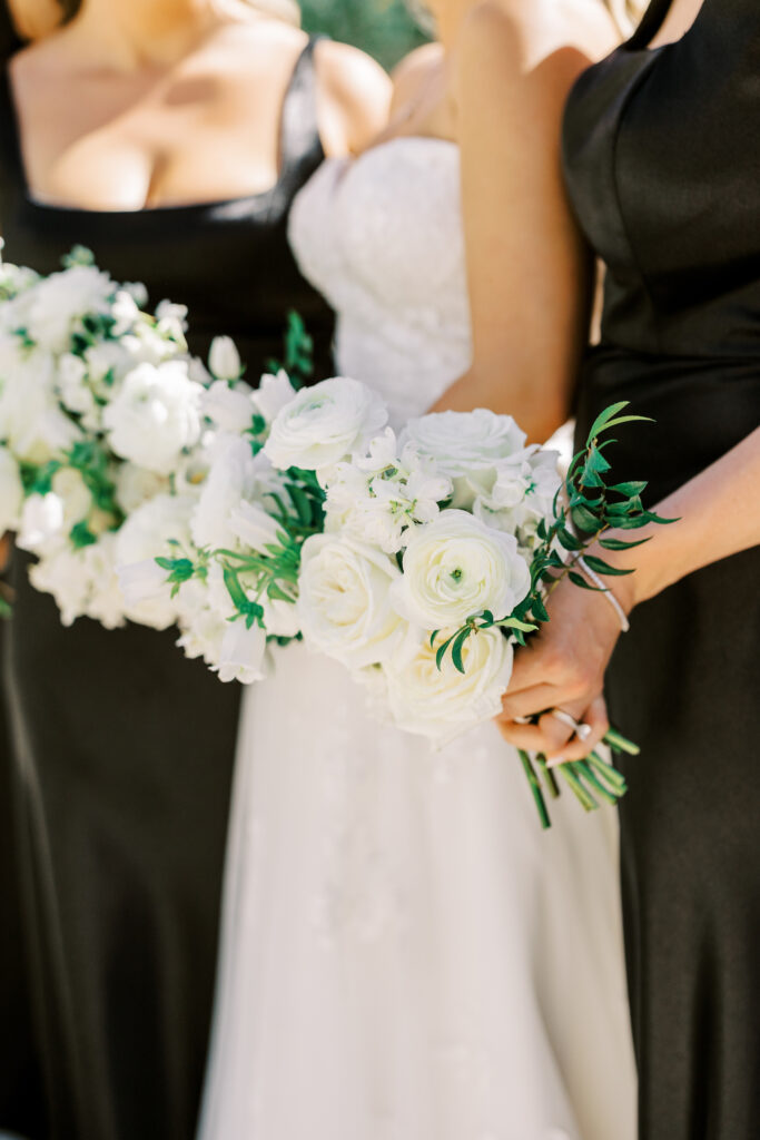 Bride standing with bridesmaids in black dresses, all holding bouquets of white flowers.