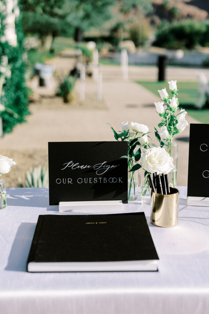 Guestbook table with white flowers bud vases and a black book.