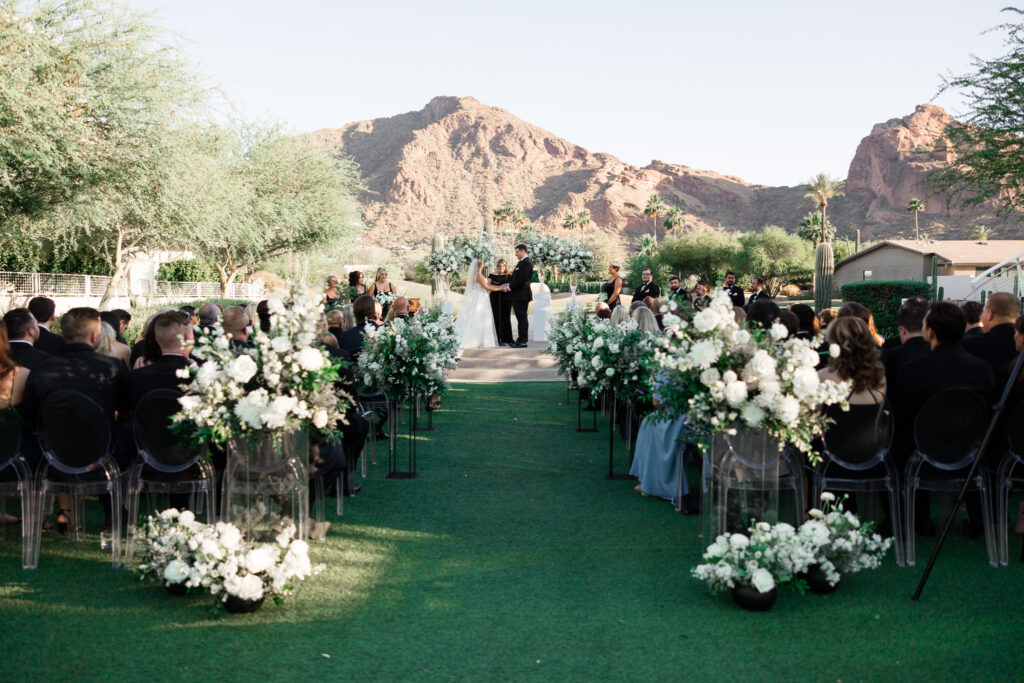 Outdoor wedding ceremony with desert mountain views at Mountain Shadows with aisle floral arrangements and bide and groom framed by floral on pillars in altar space.