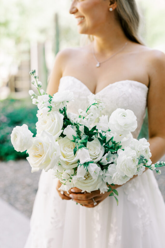 Bride holding white flowers bouquet, looking over shoulder, smiling.