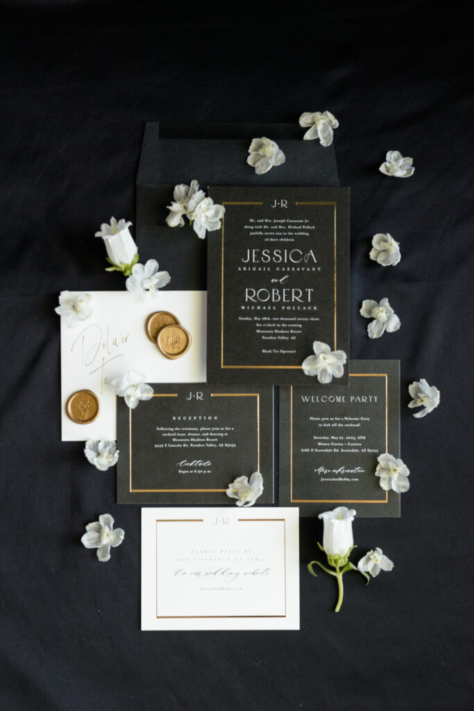 Black and white with gold accent wedding invitation suite flat lay with white flowers detail.