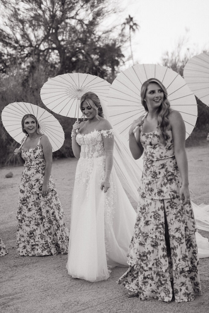 Bride with bridesmaids walking holding white paper umbrellas.