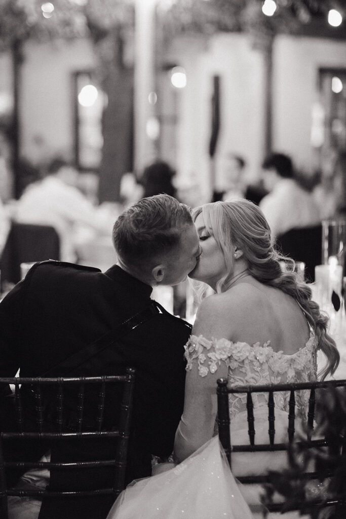 Bride and groom sitting at reception table, kissing.