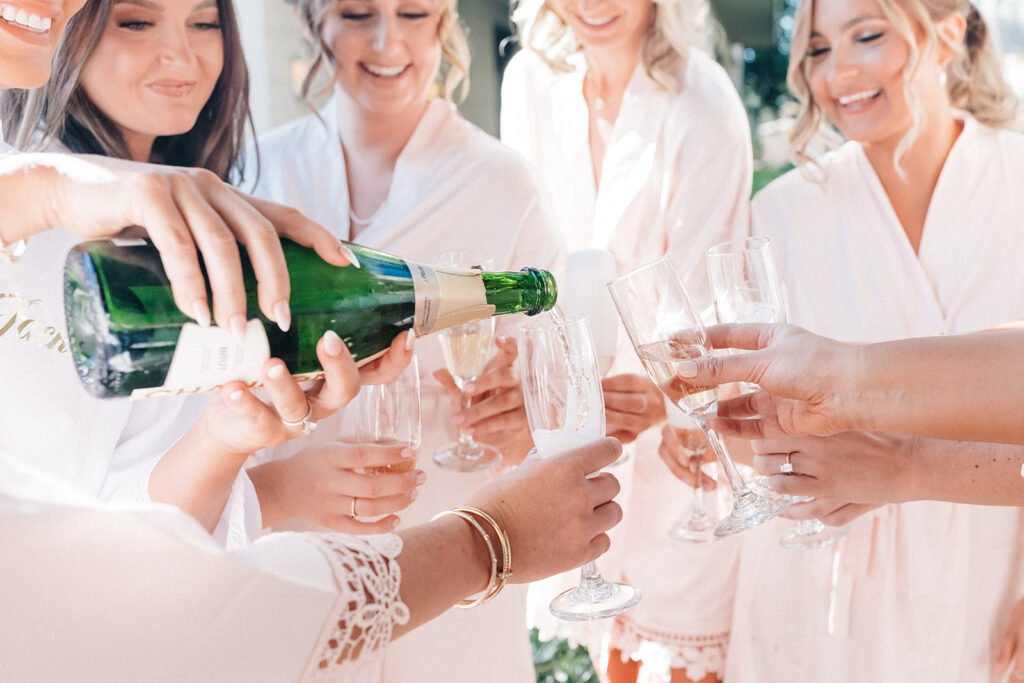 Women in bathrobes holding champagne glasses while champagne is poured into them.