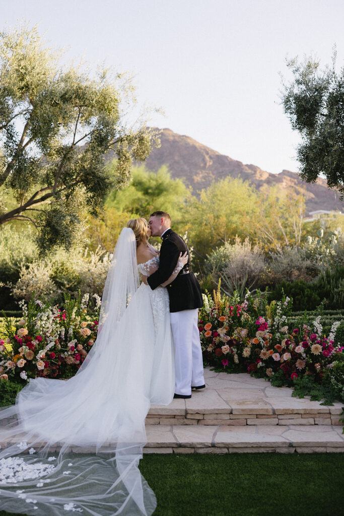 Bride and groom kissing in outdoor wedding reception altar space at El Chorro with ground floral arc behind them.