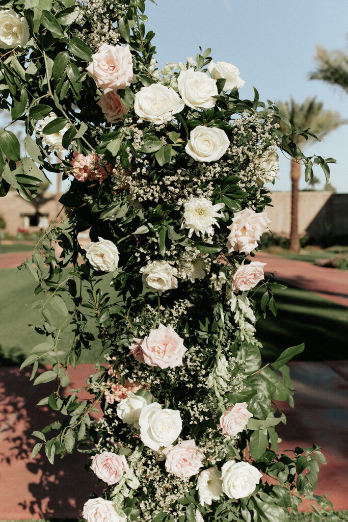 Detail image of wedding ceremony arch of white and blush flowers and greenery.