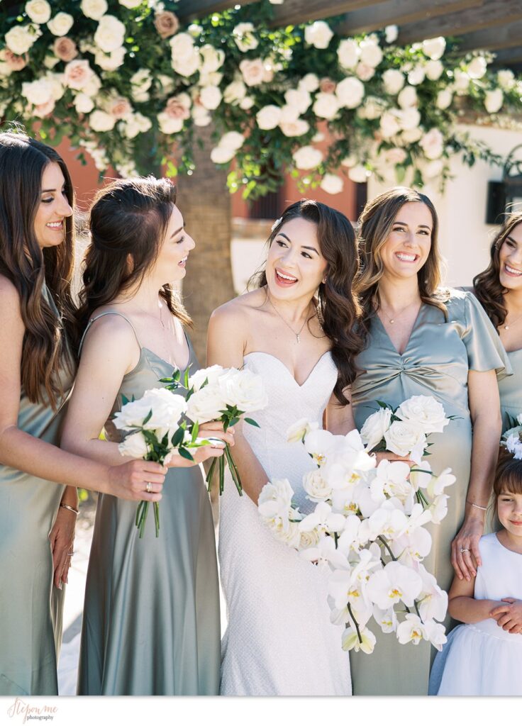 Bride with bridesmaids holding white flowers bouquets, smiling.