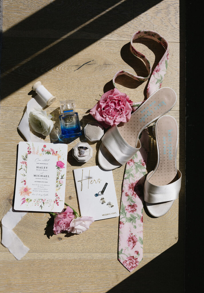 Flat lay of wedding invitation, bridal shoes, jewelry, perfume and flower tie.
