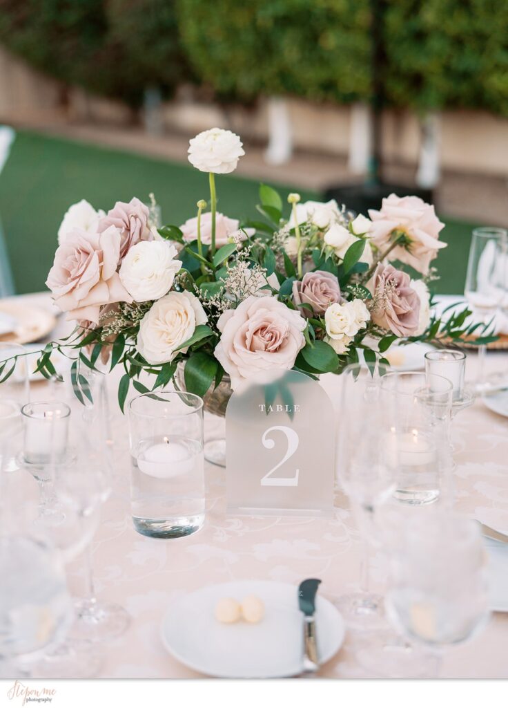 Floral centerpiece of white and blush, mauve roses in glass vase.