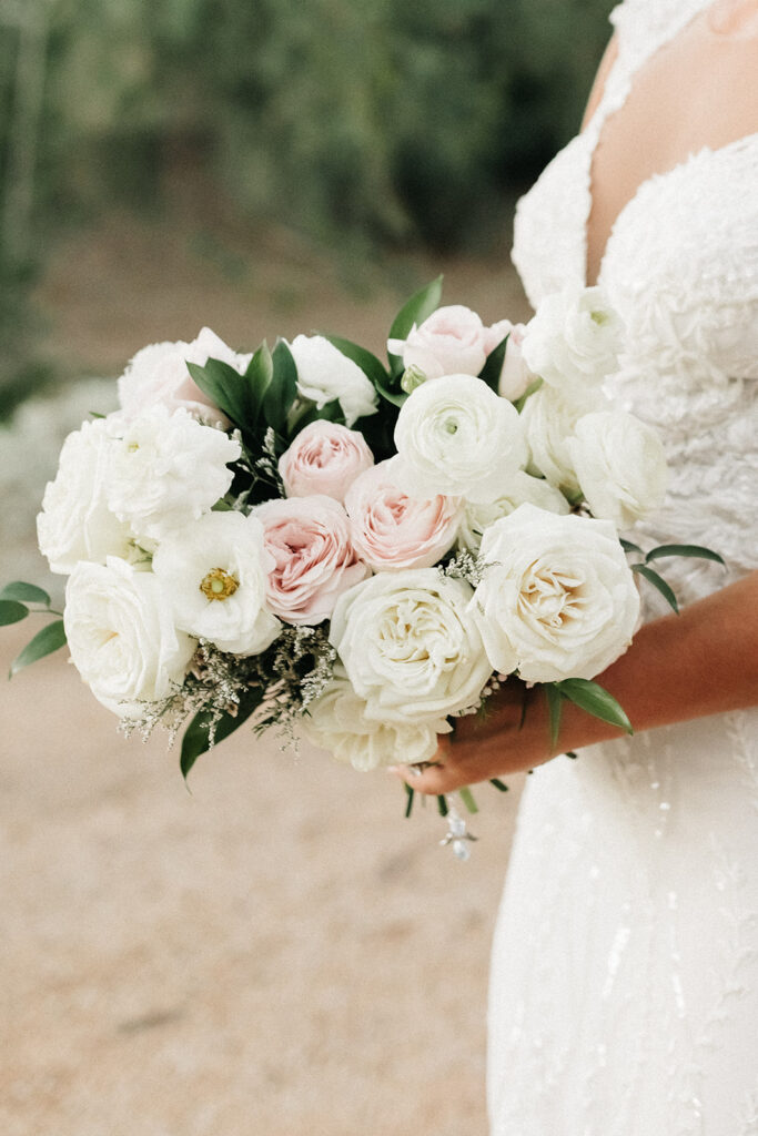 Bride holding bouquet of white and blush flowers with limited greenery.