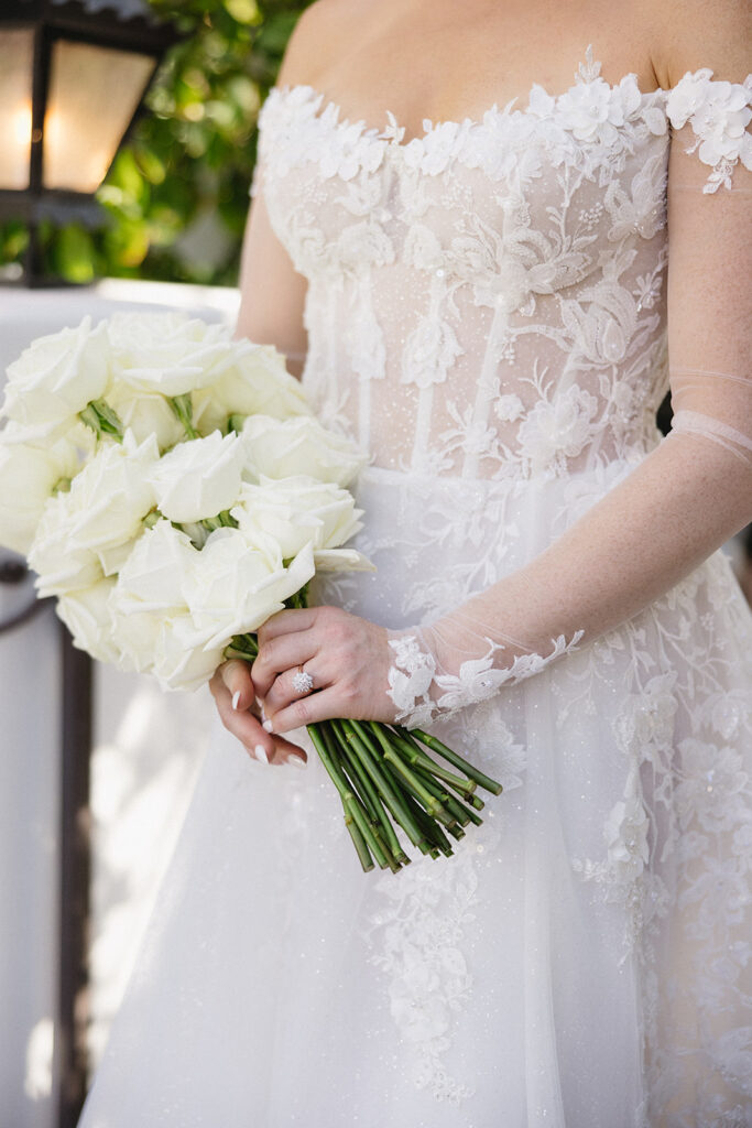 Bride in bridal gown and holding bouquet of white roses.