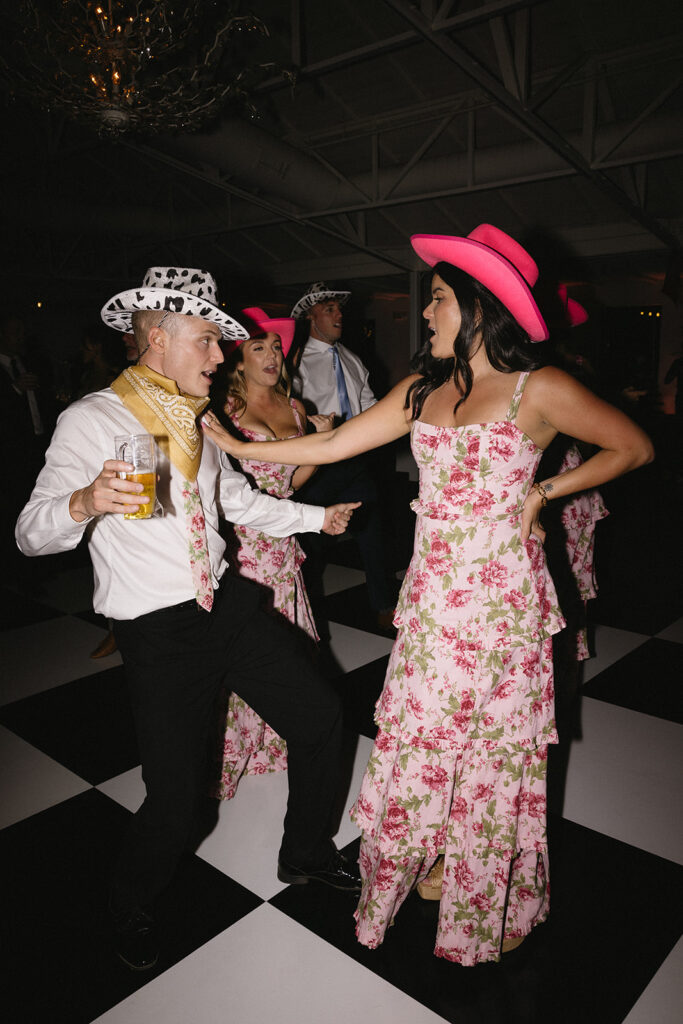 Wedding guests dancing on dance floor at El Chorro reception. Girls wearing pink cowboy hats and men wearing cow pattern cowboy hats.
