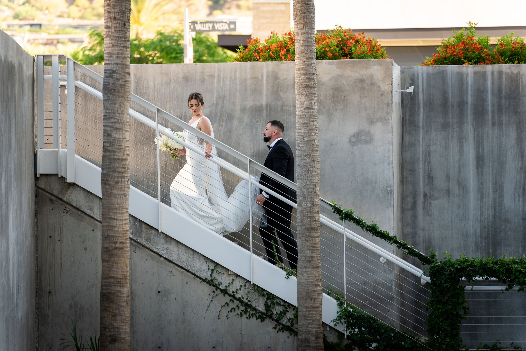 Bride ascending stairs outside at Mountain Shadows with groom ascending behind her holding train of her dress.