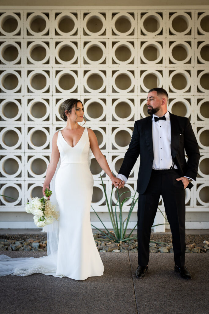 Bride and groom holding hands, looking at each other, in front of white pattern circles wall at Mountain Shadows resort.