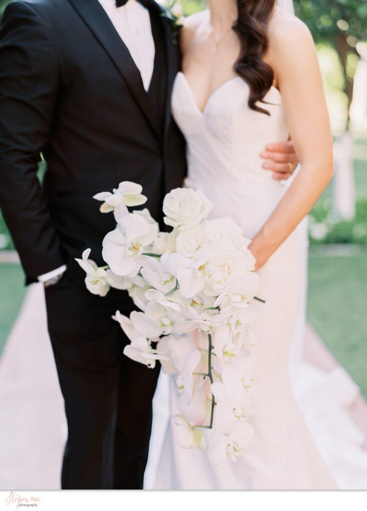 Bride holding lush bouquet of white orchids and roses.