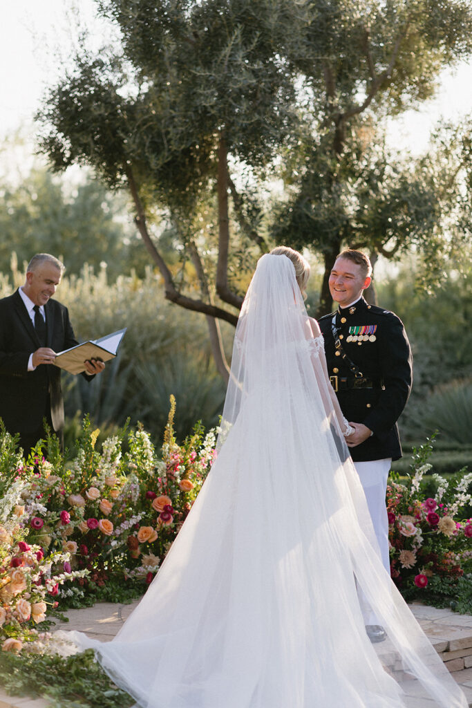 Groom smiling at bride with bride's back to camera in outdoor wedding ceremony altar space at El Chorro with ground floral arc.