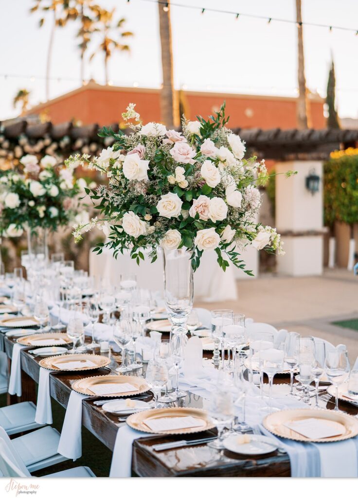Tall wedding reception centerpiece of white and blush, mauve flowers in glass vase at long reception table.