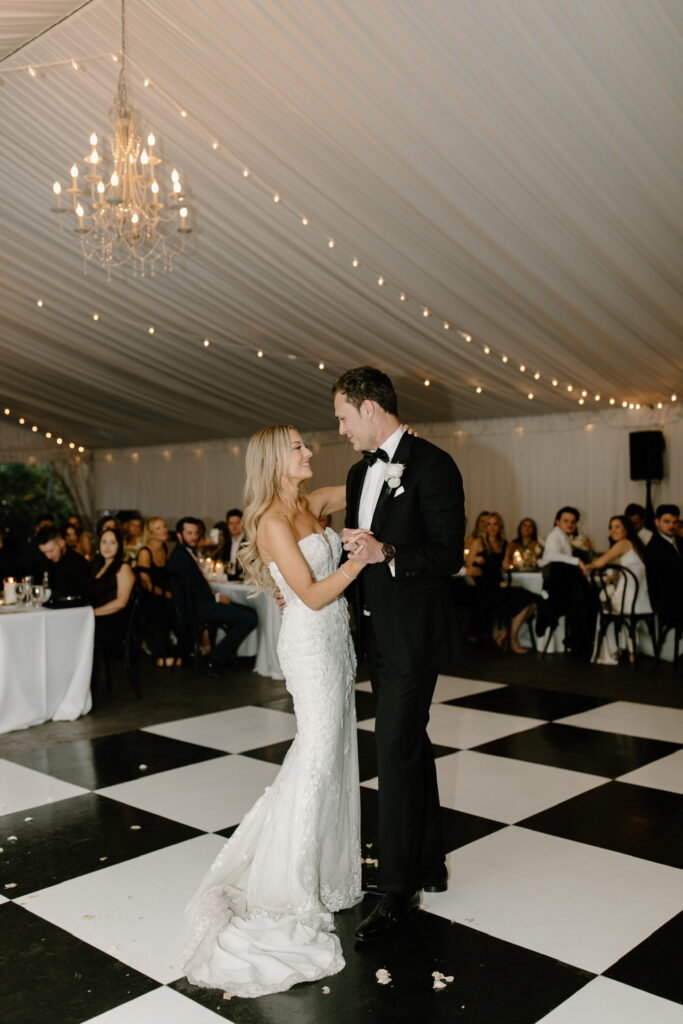Bride and groom dancing at wedding reception on black and white checkered floor.
