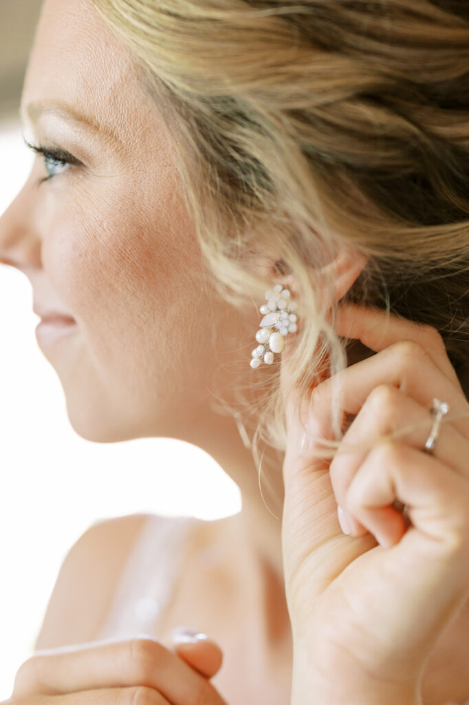 Bride putting on earring of white beads.