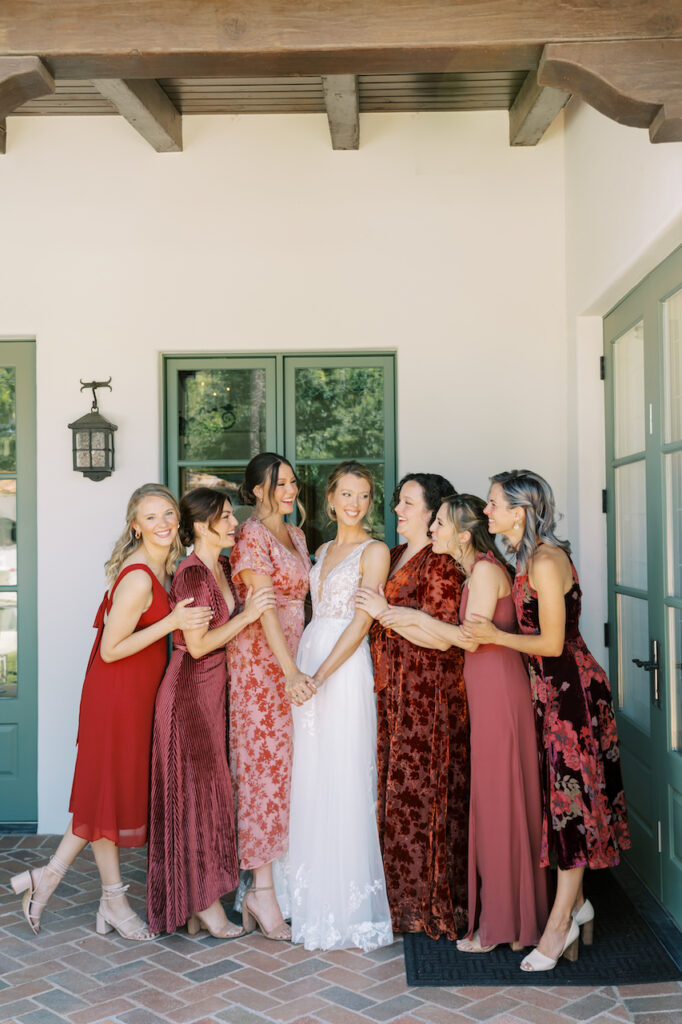 Bride standing in center with bridesmaids leaning in towards her, all smiling.