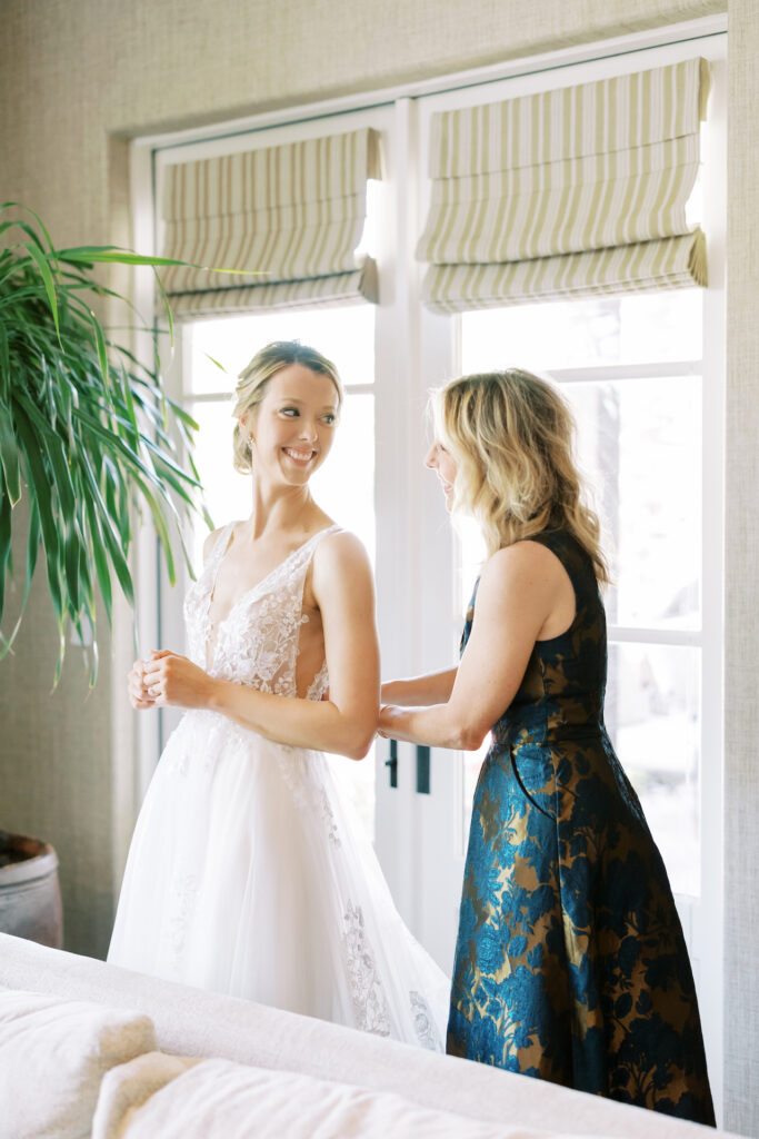 Woman helping bride into her gown, bride smiling over her shoulder.