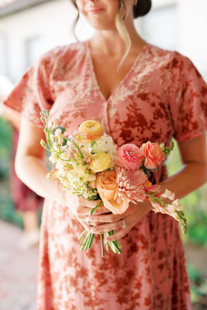 Bridesmaid in pink-red gown holding bouquet of white, pink, yellow, orange, and peach flowers.