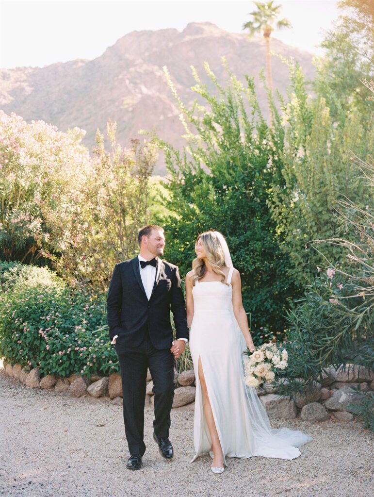 Bride and groom holding hands, smiling at each other standing in desert landscape.