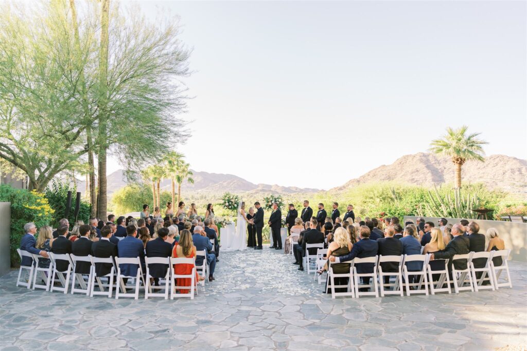 Outdoor wedding ceremony with guests seated and wedding party up front with bride and groom in altar space with officiant.