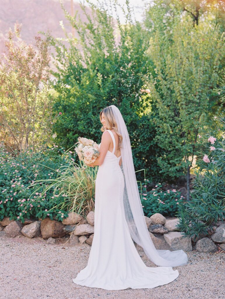 Bride holding and looking down at bouquet standing in desert landscape.