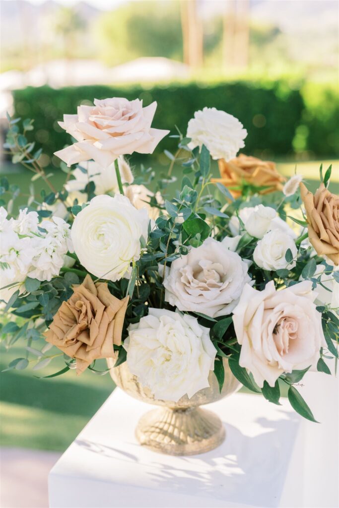 Low floral arrangment in brass vase of white, blush, and gold roses with greenery.