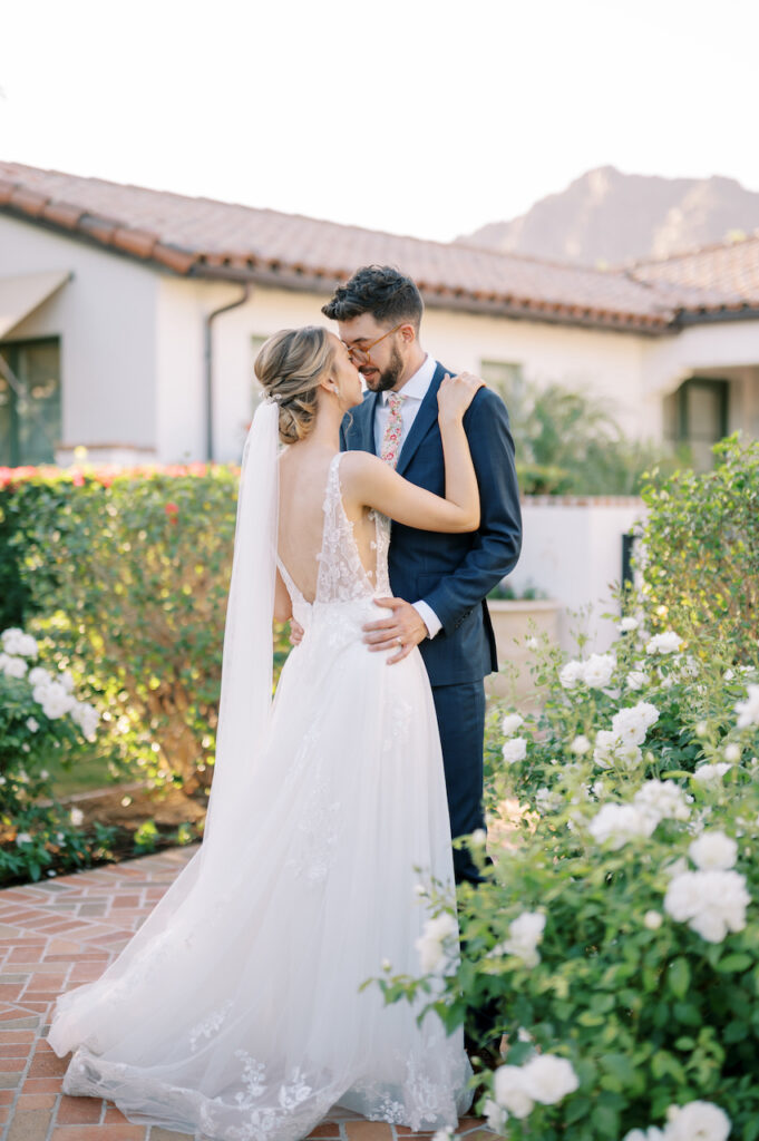 Bride and groom embracing with rose bushes in landscape and mountain in background.