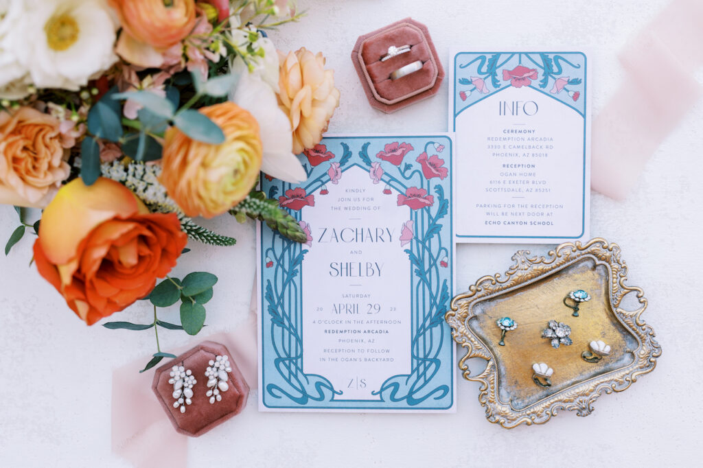 Wedding invitation flat lay with bouquet, rings, and earrings.